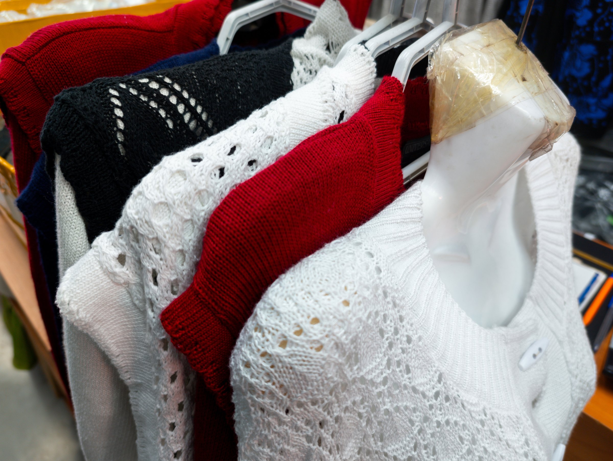 Several knit sweaters in different colors are arranged on hangers in a store. The sweaters feature distinct patterns and textures, showcasing the variety available for customers.