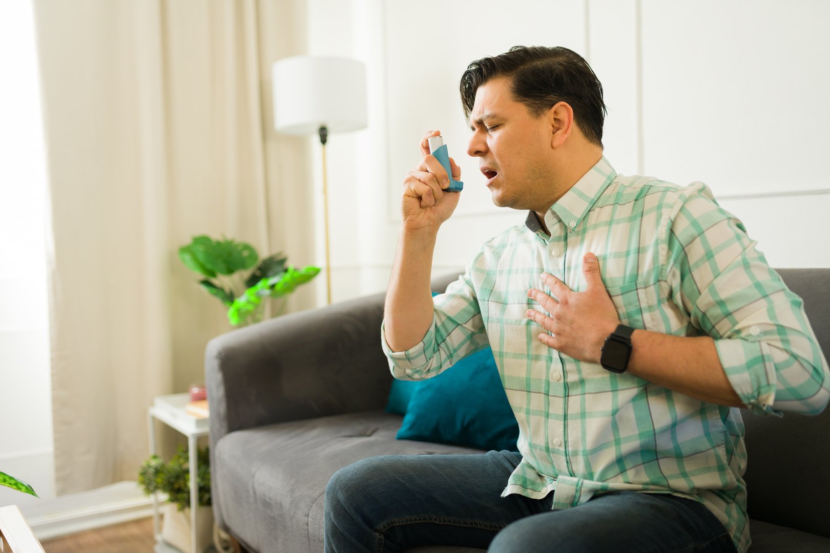 Asthmatic latin male experiencing respiratory distress, using inhaler and pressing hand against chest during breathing difficulty