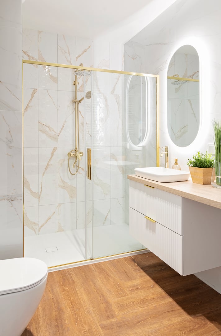 Home interior with ceramic bathroom sink on cupboard with gold water tap and shower with glass and mirror on the wall.  Interior decor.