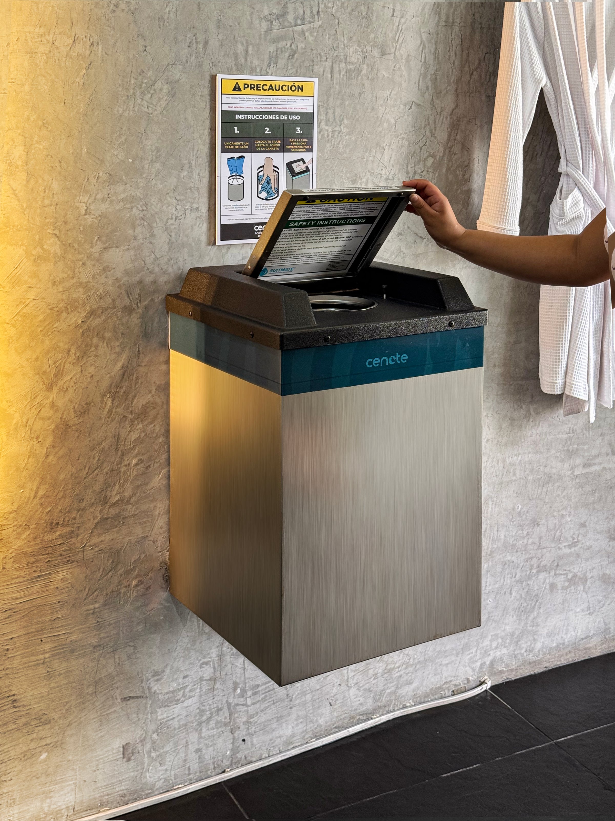 Person using a modern stainless steel towel disposal unit mounted on a wall with an instruction sign above.