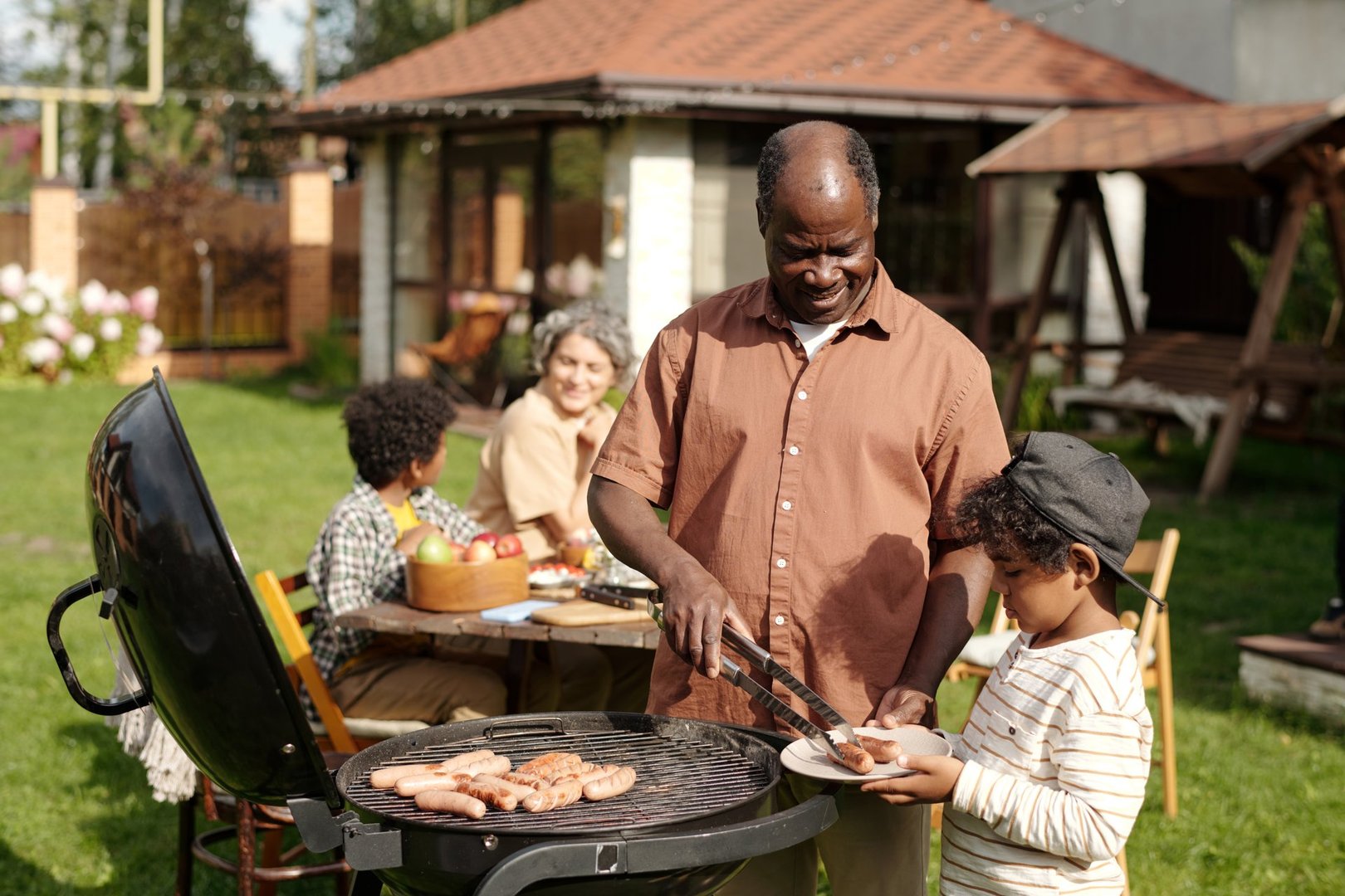 Family enjoying an outdoor barbecue with senior man grilling food accompanied by a child. Multigenerational group having fun and sharing a meal in a backyard setting