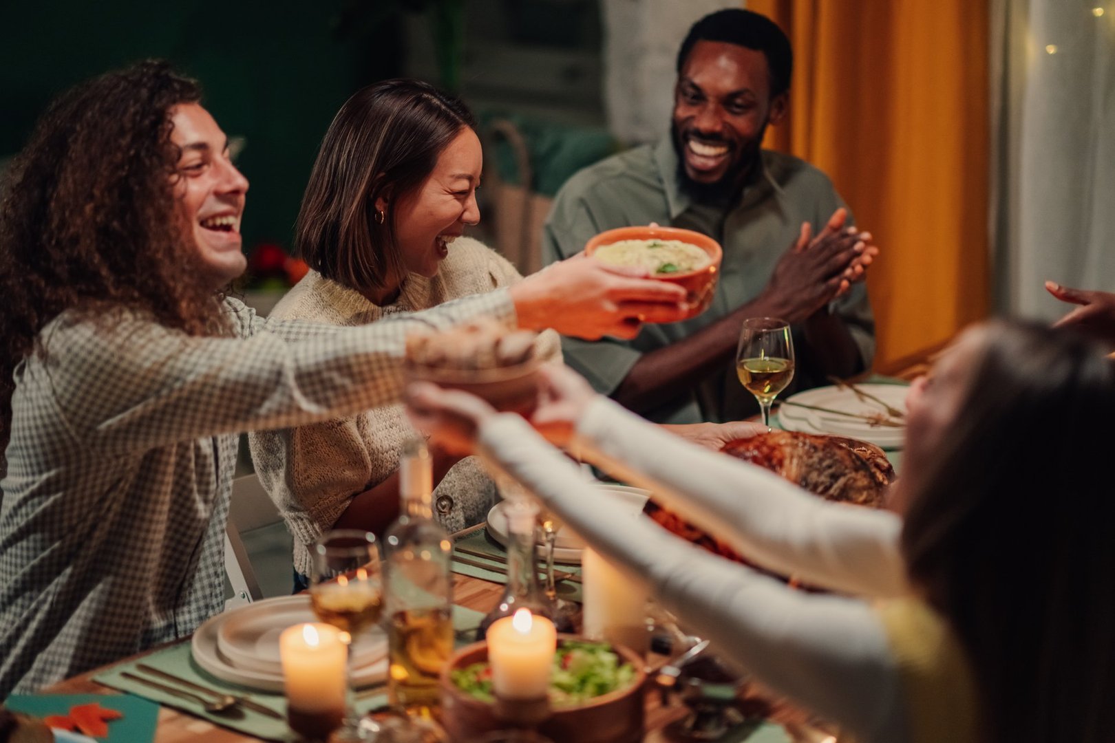 Cheerful friends passing food across the table at a thanksgiving dinner, enjoying the festive meal together