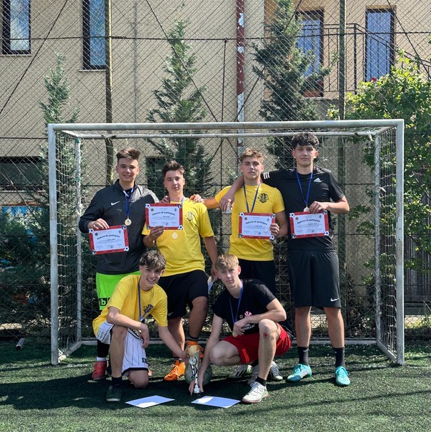 Six young men on a football field posing with certificates and medals in front of a goal.