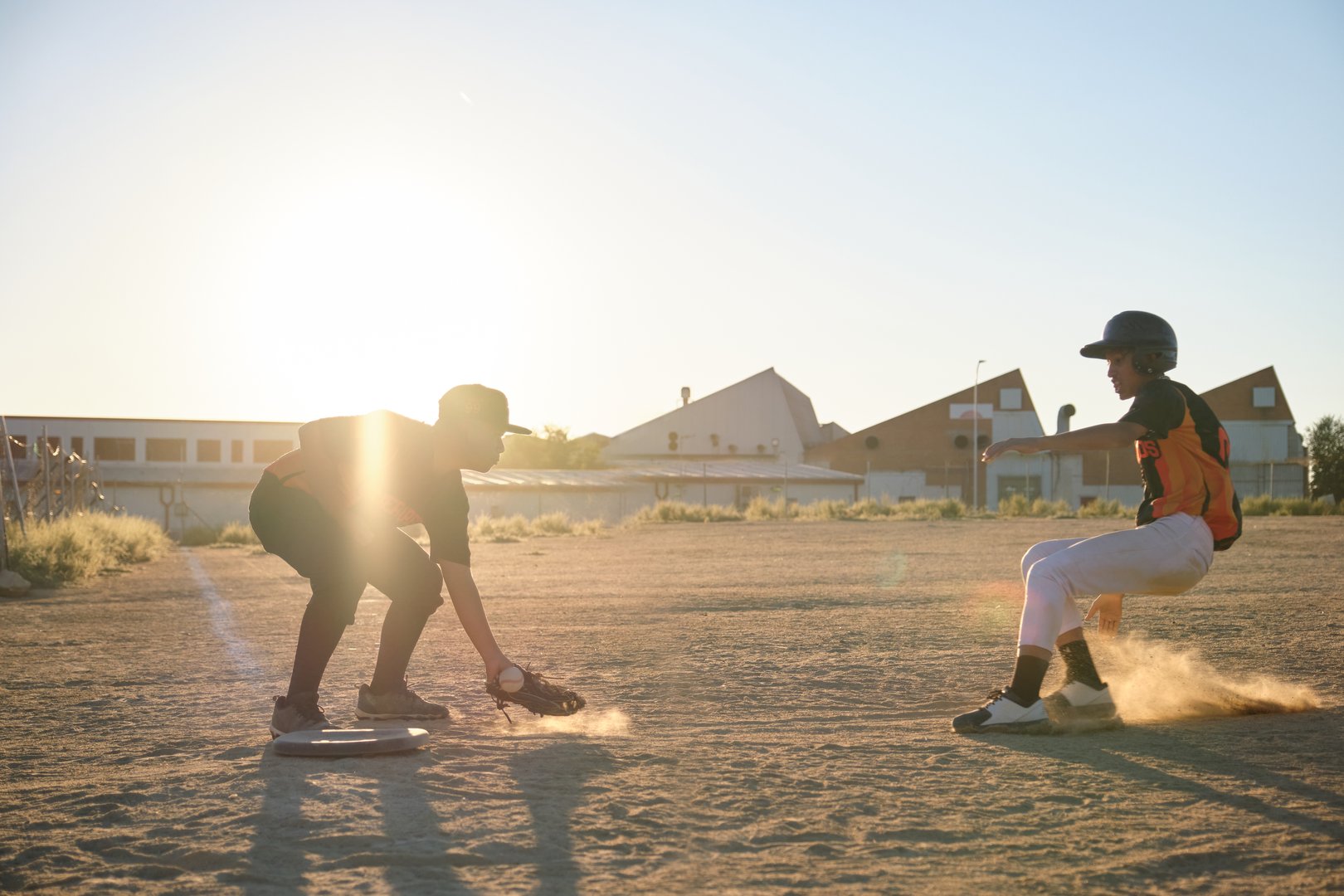Two boys playing baseball on a dusty field at sunset