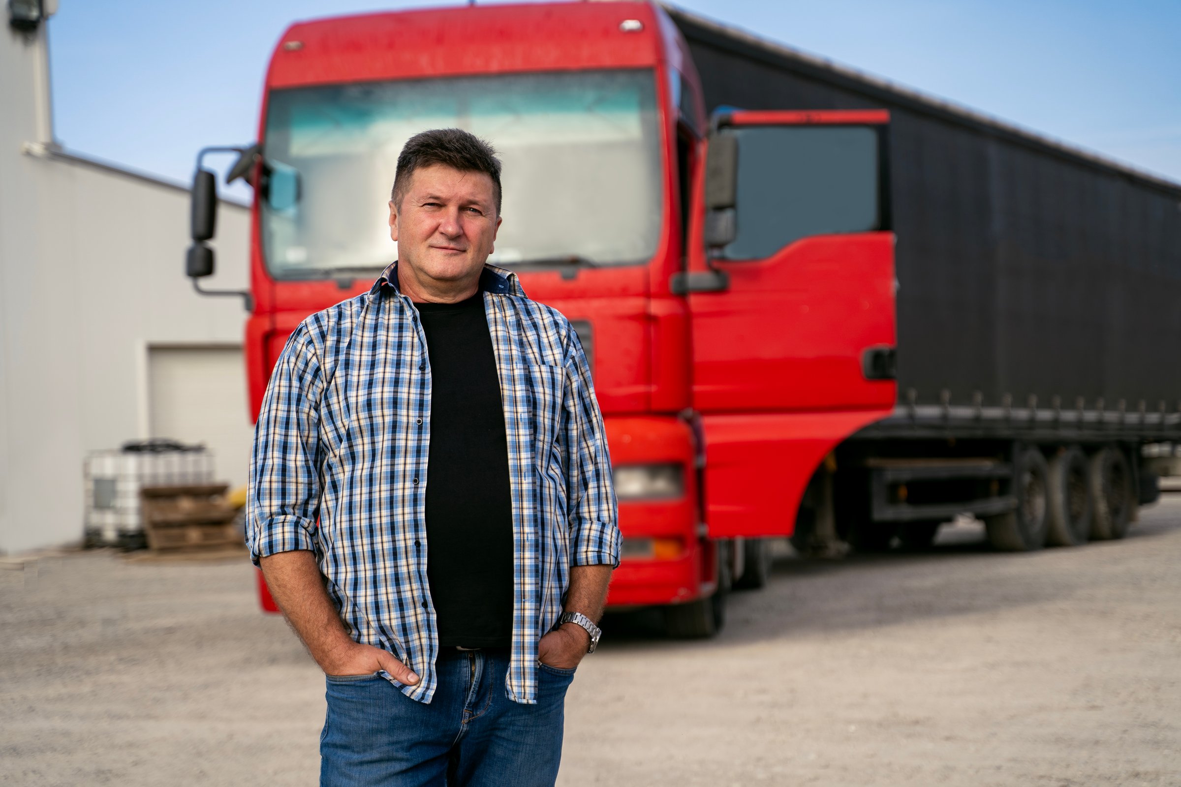 Middle age Caucasian truck driver standing confident in front of his vehicle, hands in pockets