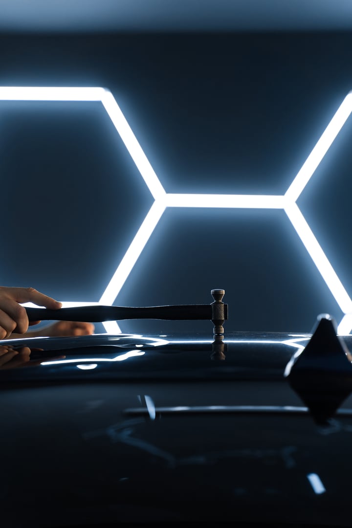 Paintless dent repair PDR involves tapping dents under light reflection for precision. Technician uses PDR tools to remove dents from a car hood during paintless dent repair