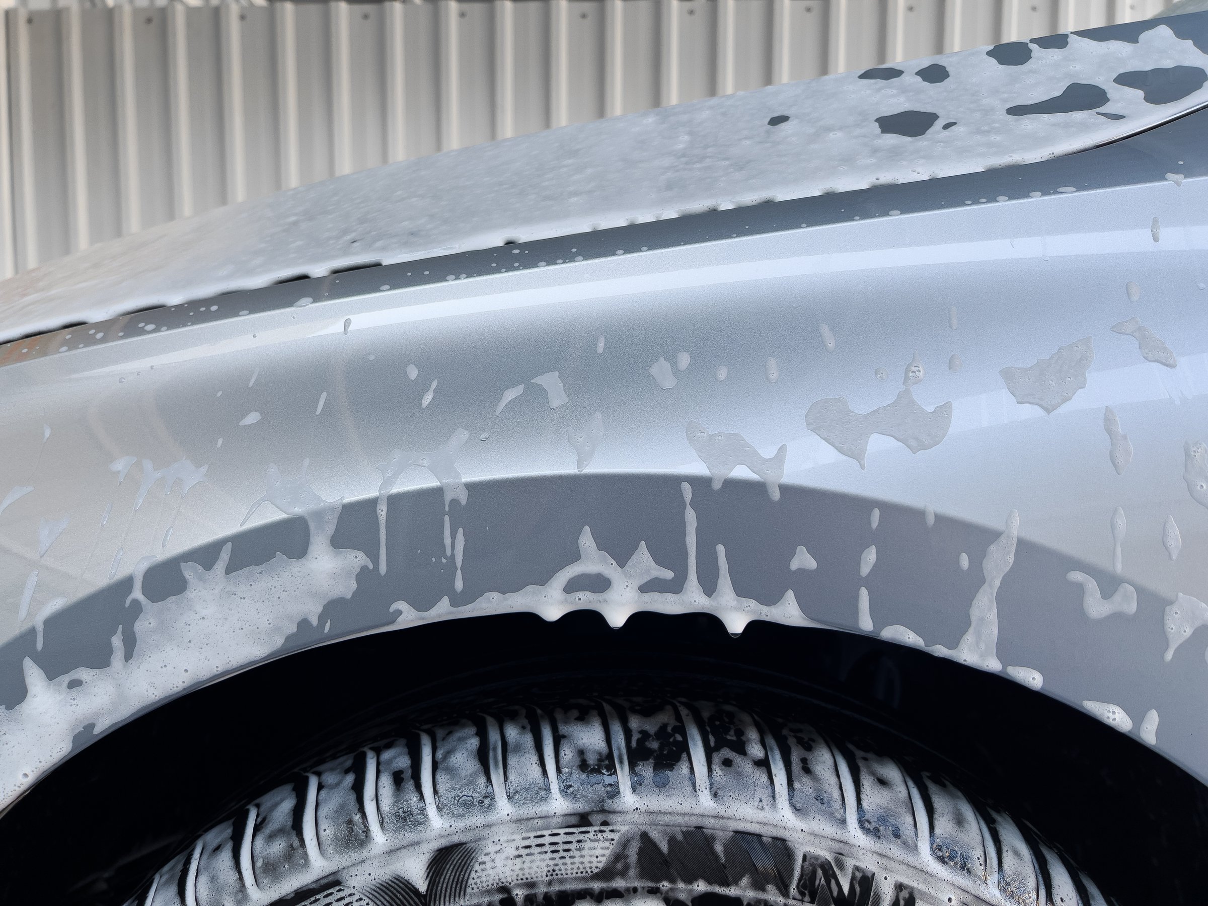 Grey car washing with white soap foam, taken on mobile device