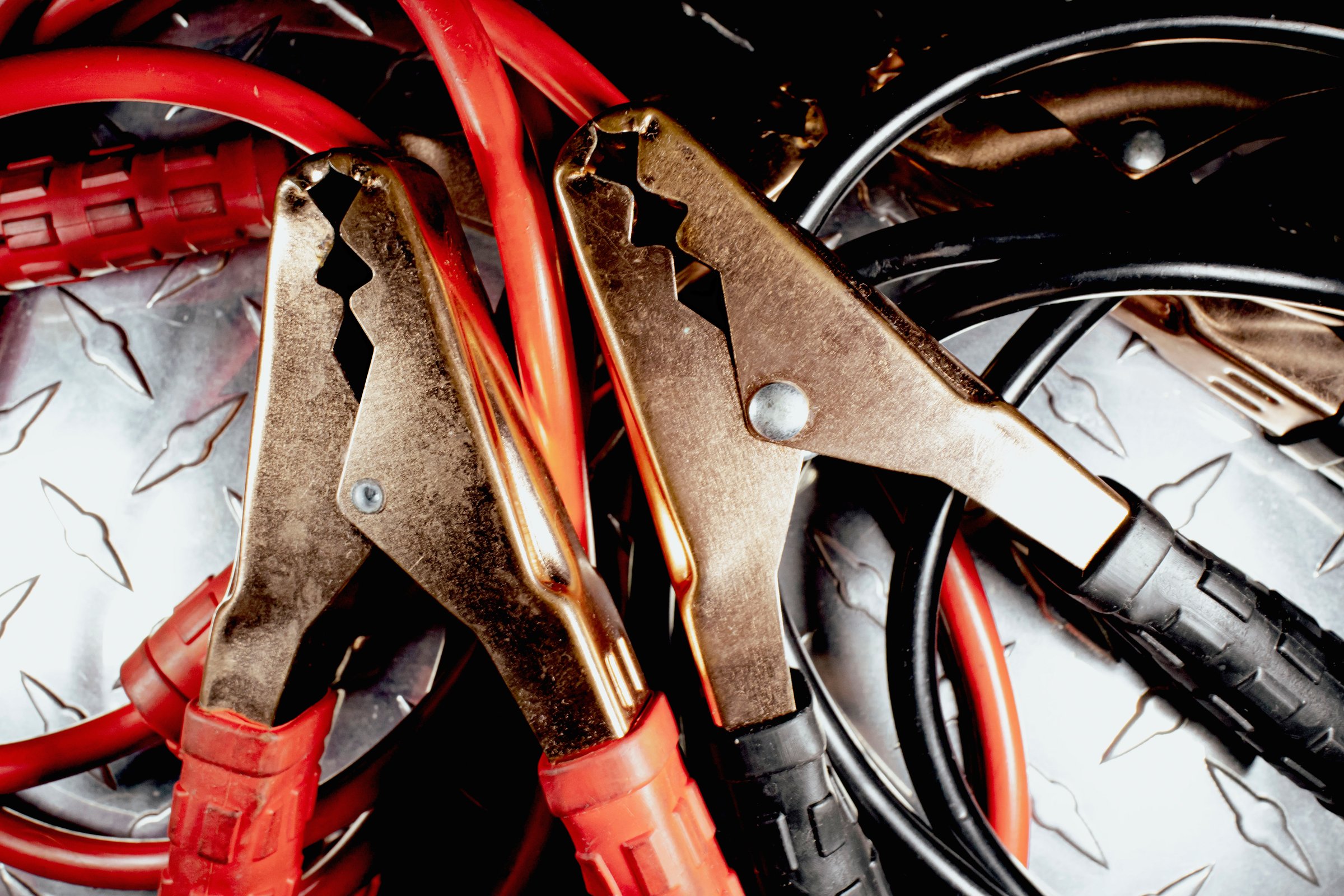 Piled on a diamond plate metal surface, red and black jumper cables with gold clamps sit ready for jump-starting a vehicle, providing essential power for automotive emergencies