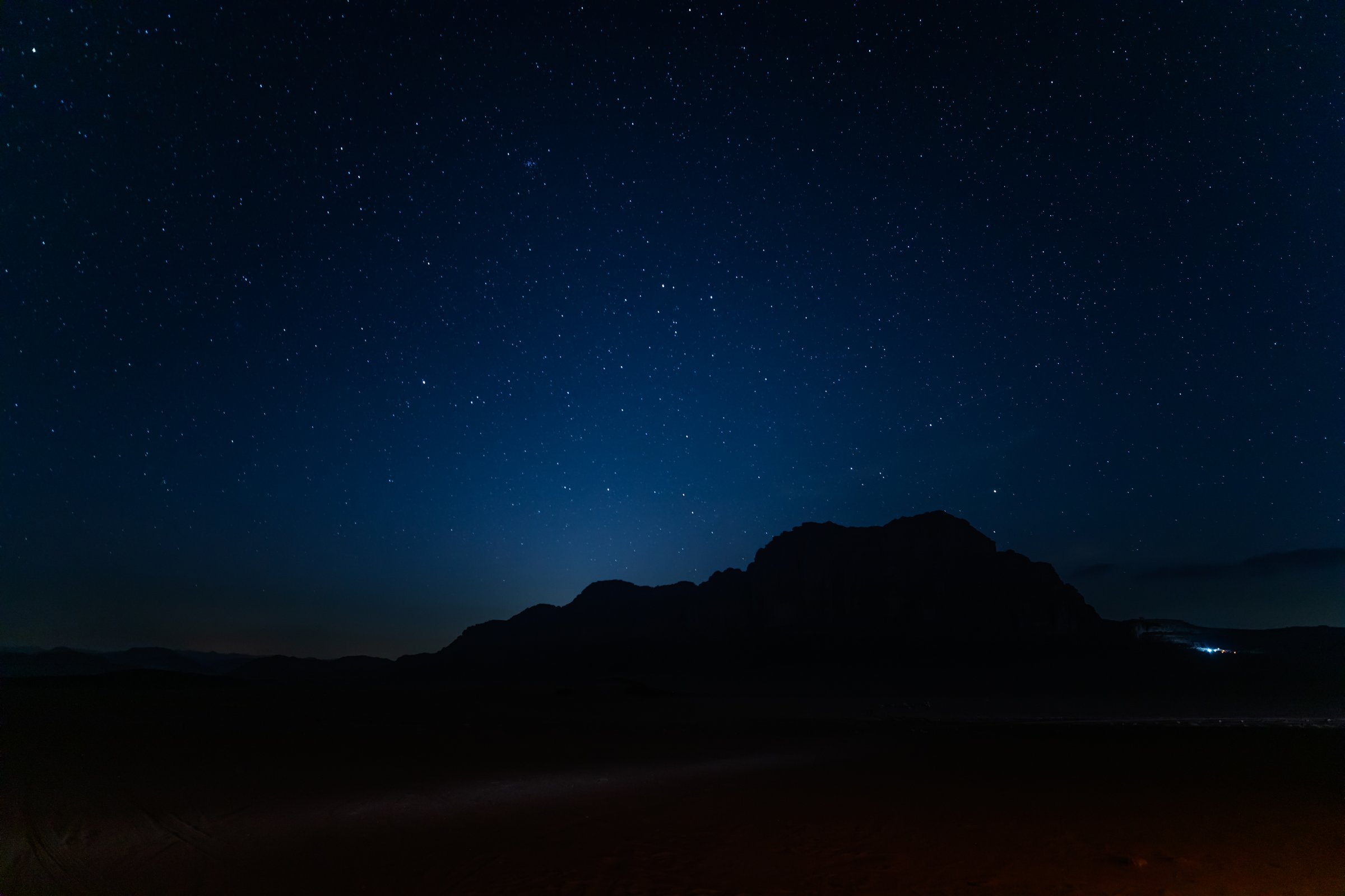 Captivating night sky, sprinkled with stars sets over the silhouette of Jabal al Qattar rock formation in the tranquil Wadi Rum desert in Jordan in April