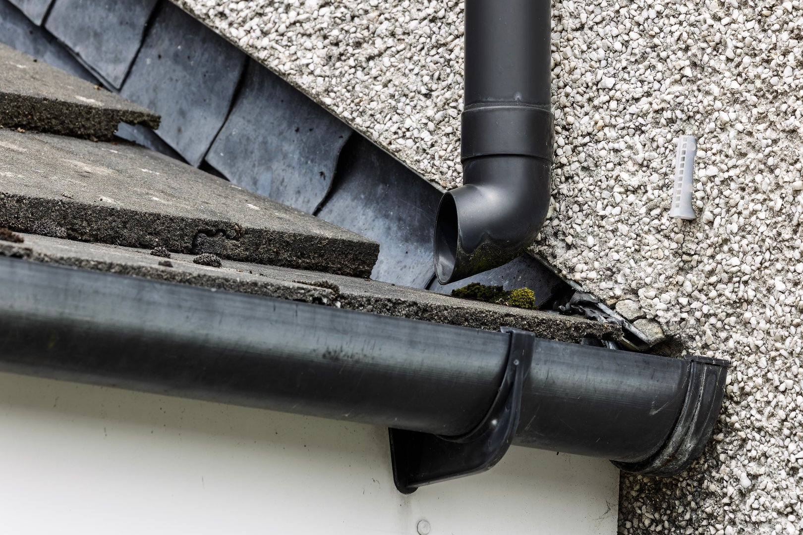Black plastic rainwater downpipe and guttering attached to a residential house