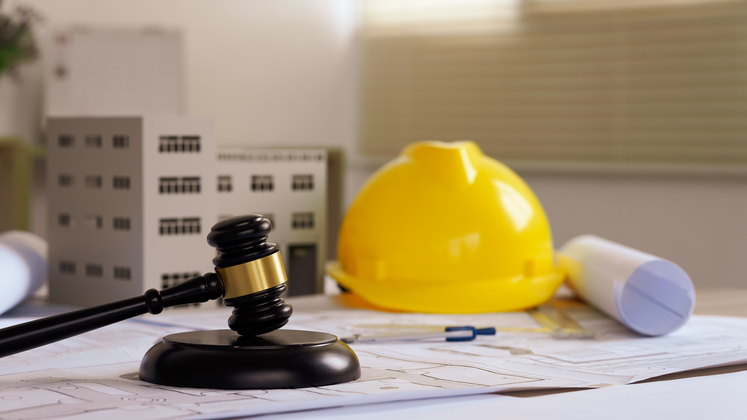 Judge gavel on building blueprint plans with a yellow safety helmet in the background. law that deals with matters relating to building construction, engineering. Construction law concept.