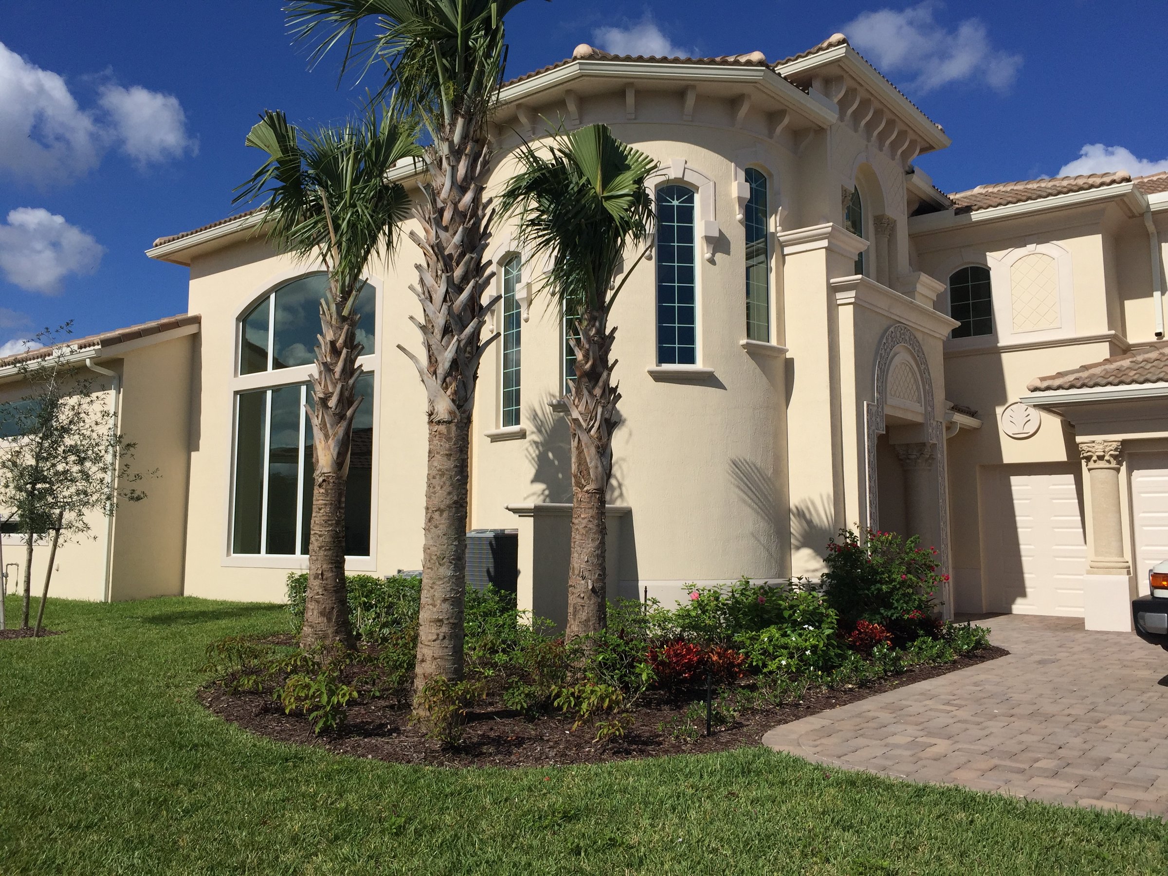 Large Mediterranean-style house with palm trees, beige stucco walls, arched windows, and a tile roof under a blue sky.
