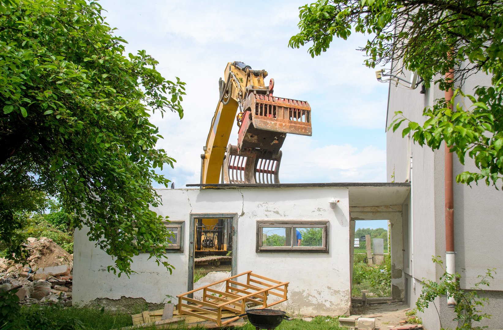 excavation bucket working at the demolition of an old garden building