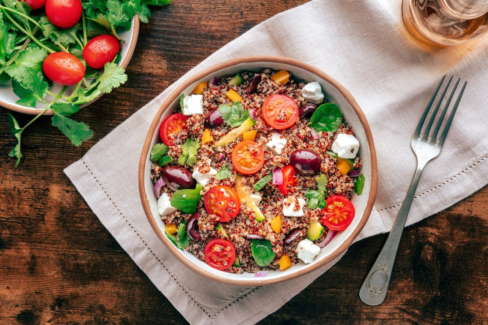 Quinoa salad, healthy Mediterranean lunch with fresh organic vegetables, cheese, and olives, overhead flat lay shot on a rustic wooden background