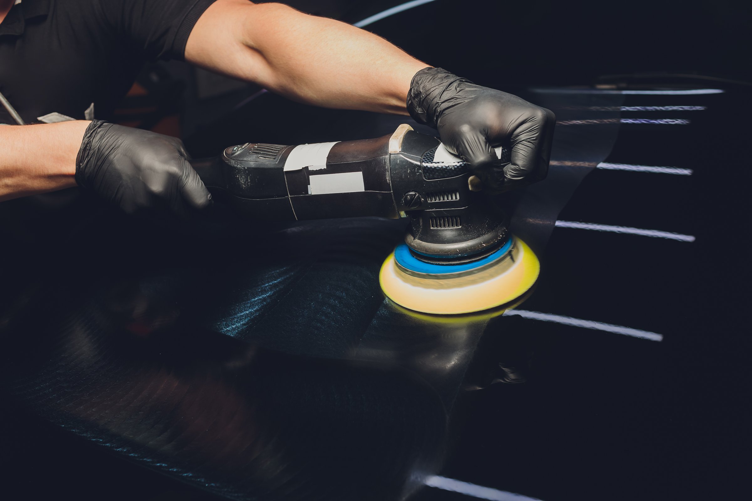 Car detailing - Hands with orbital polisher in auto repair shop. Selective focus