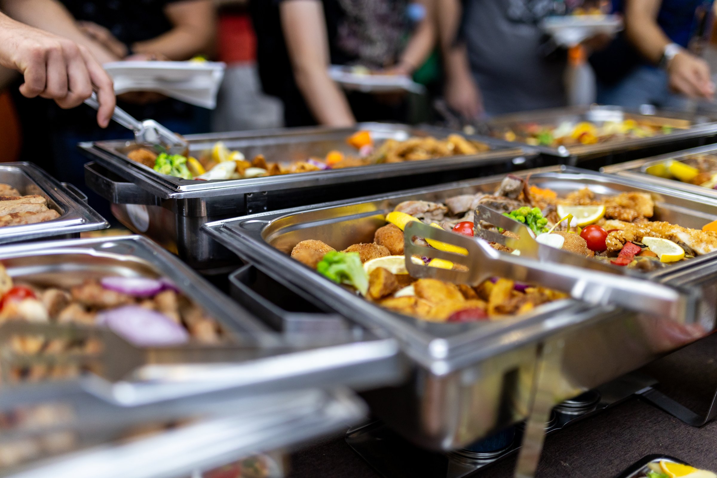 Guests are serving themselves from a beautiful buffet featuring a variety of colorful dishes and appetizers in a festive indoor setting.
