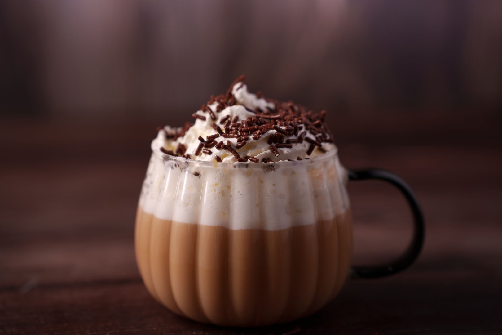 warm coffee beverage topped with whipped cream and chocolate sprinkles in a glass cup with a dark background, creating a cozy and inviting atmosphere, velvety, rich, satisfying, joyful, gourmet
