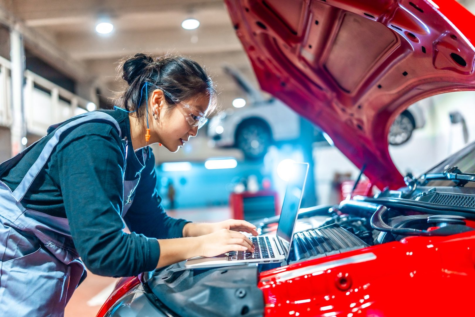 Young female mechanic using a laptop while performing diagnostics on a red car in a modern auto repair shop