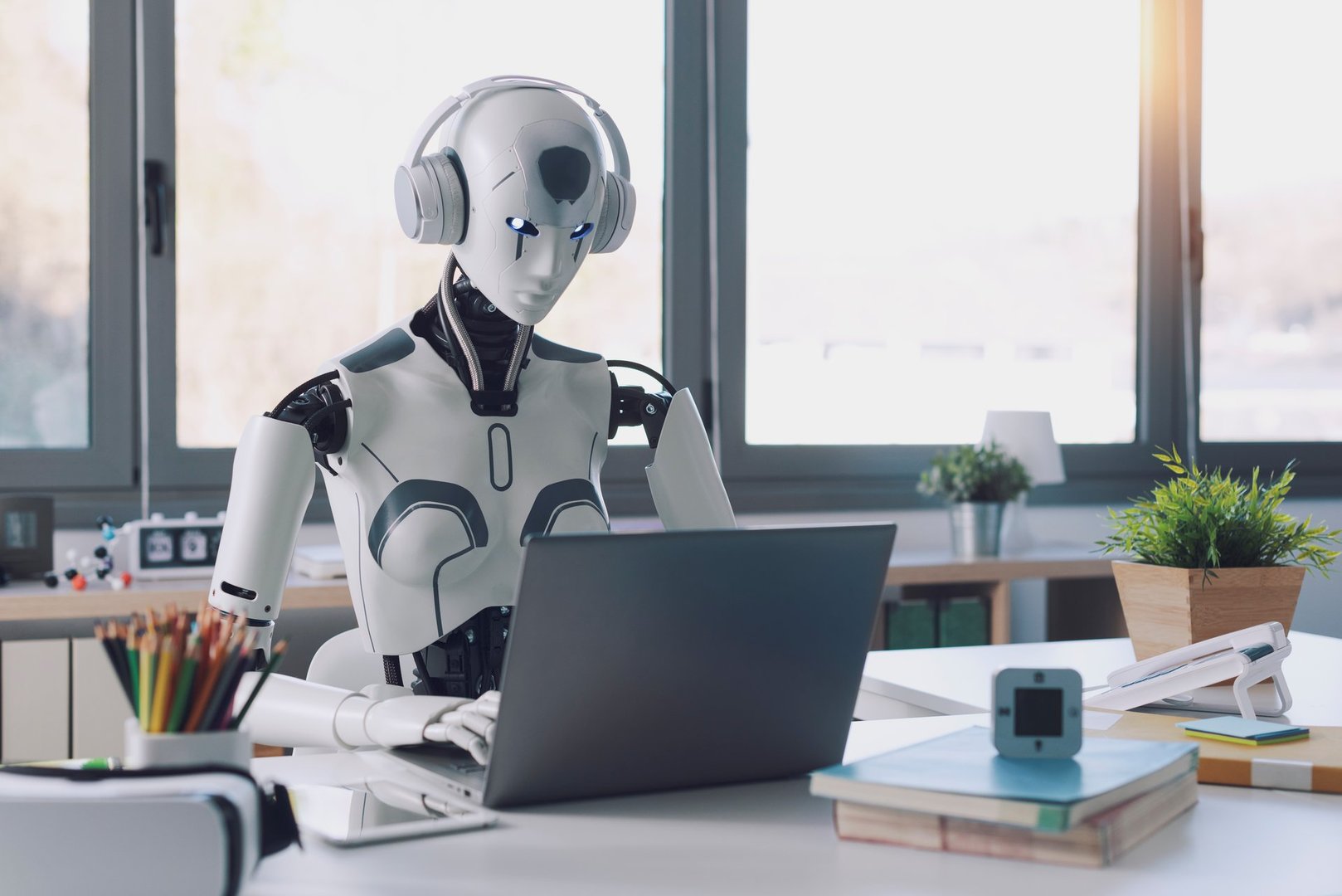 A humanoid robot works in an office on a laptop