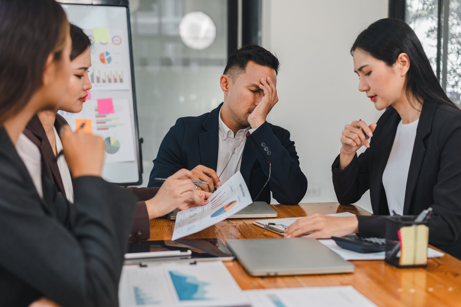 group of professionals in meeting, showing concern and frustration. man appears stressed while reviewing documents with colleagues.