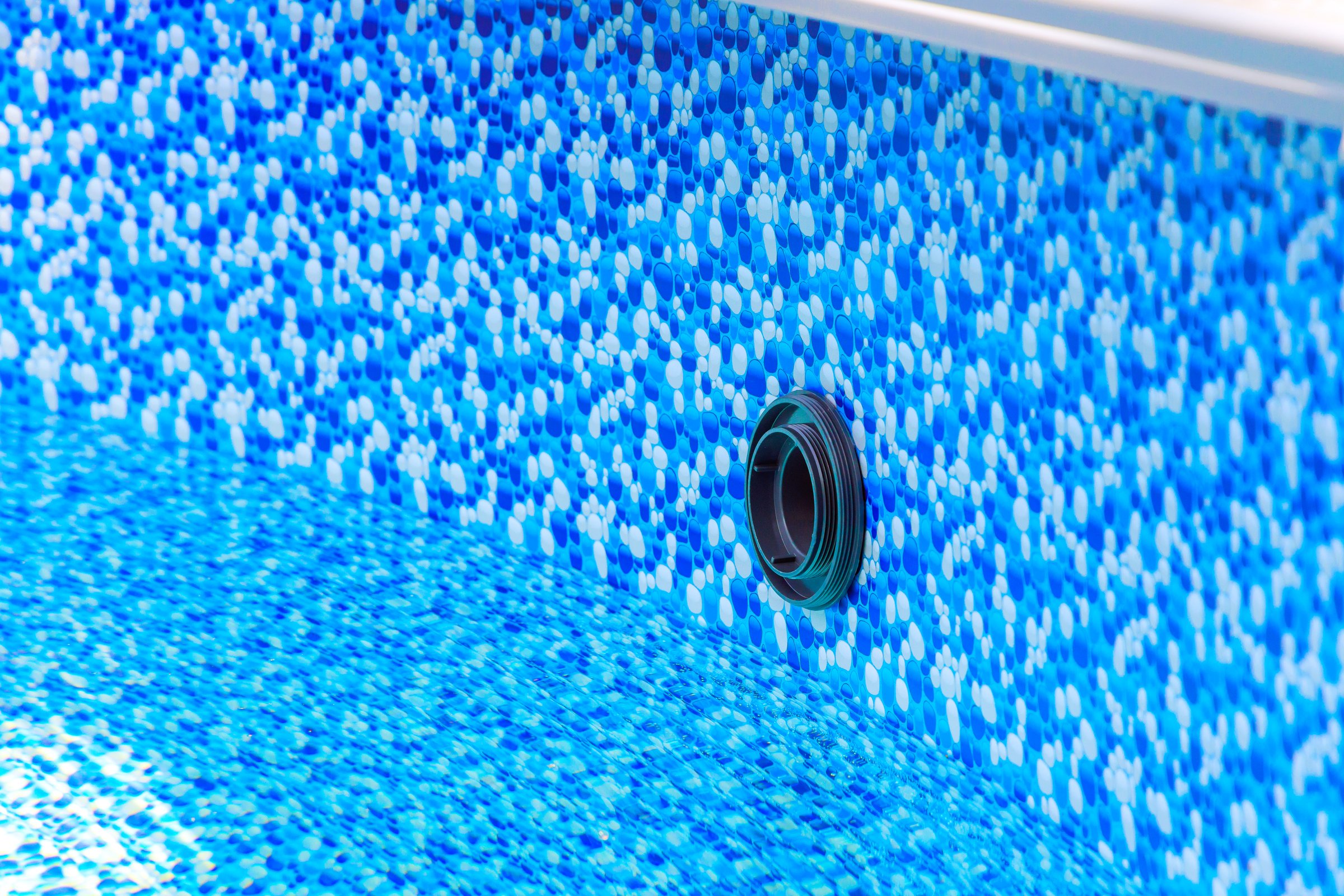 Bright blue mosaic design of pool liner reveals drainage opening in clear water