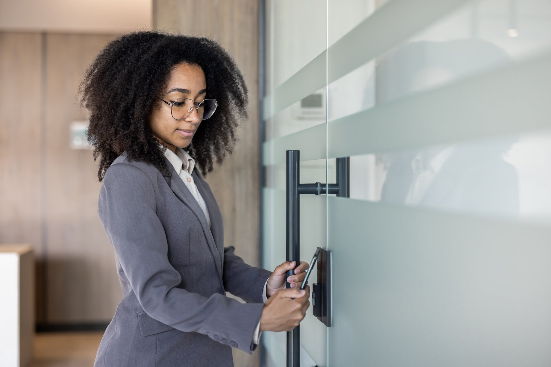 Young african american business woman enters office through electronic key, puts mobile phone to scan glass door lock.