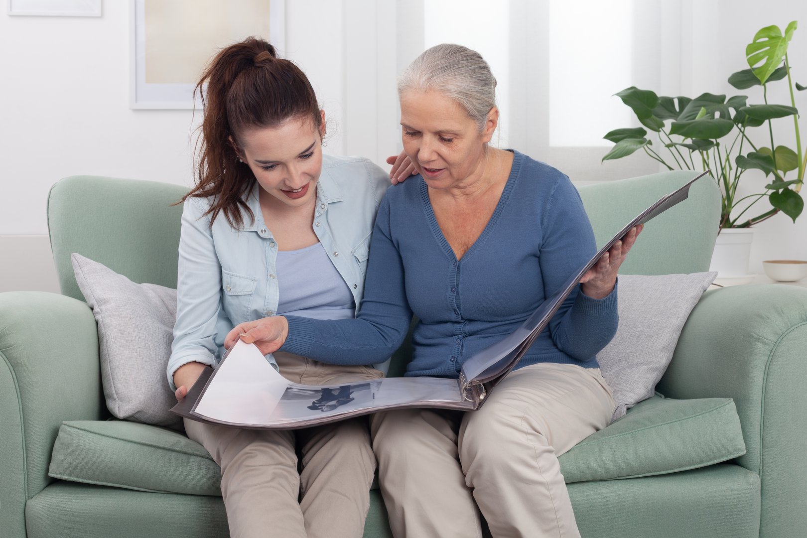 Joyful elderly grandmother sharing memories with her smiling granddaughter as they look through an old photo album together. A family moment full of connection, nostalgia, and generational bonding