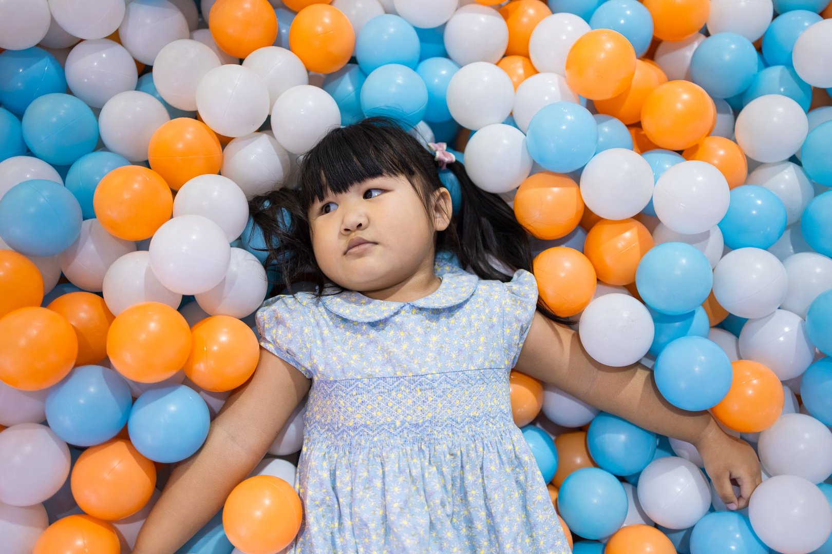 A cute young Asian girl with pigtails lying down and relaxing amidst plastic balls