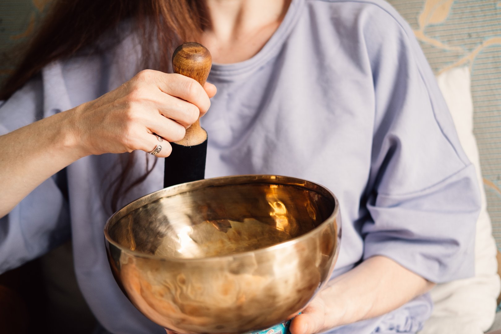 Intimate close-up of a woman's hands as she plays a Tibetan singing bowl, symbolizing mindfulness and self-care.