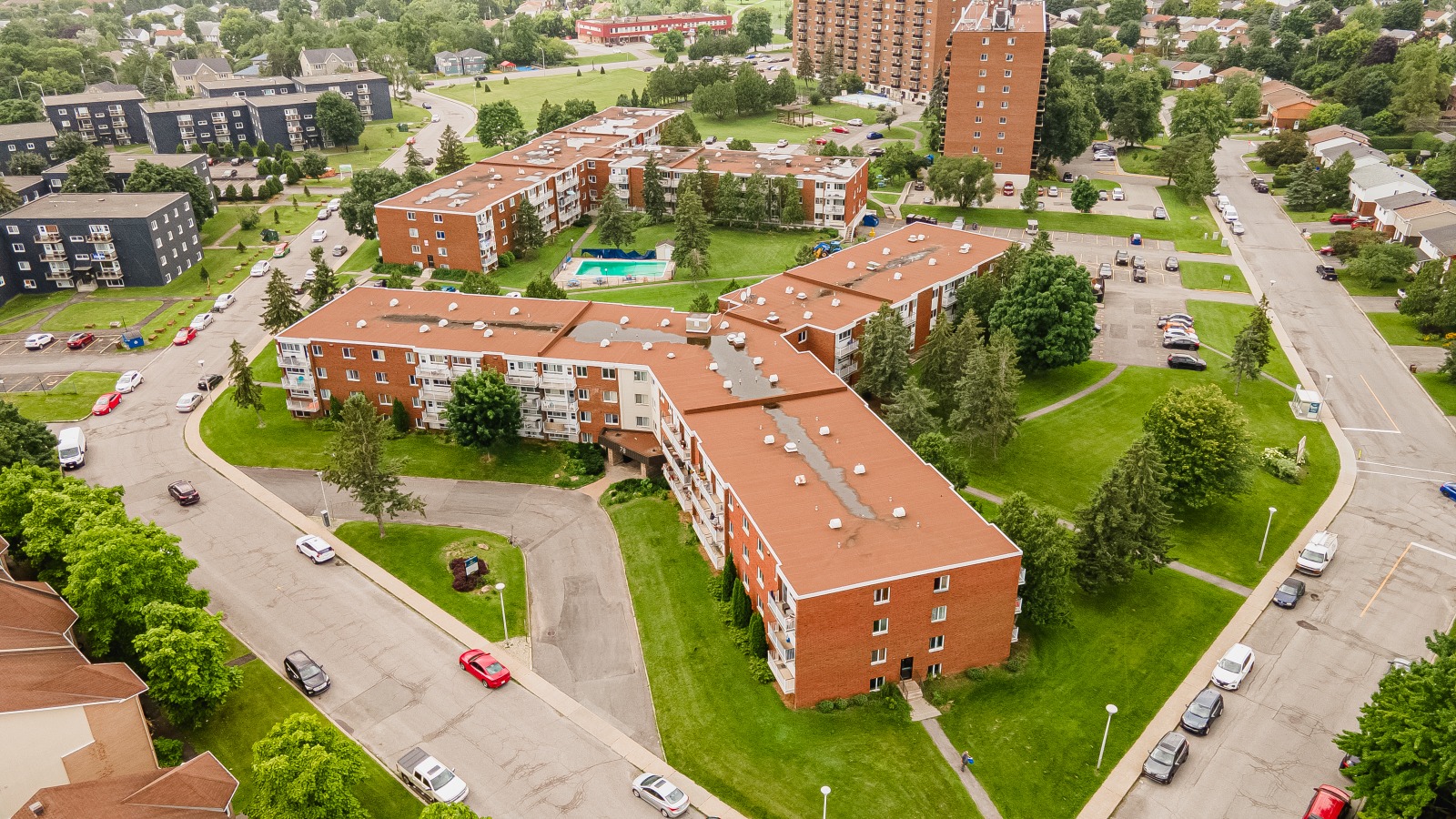 Aerial view of a residential complex with red brick buildings, a central pool, and surrounding greenery.