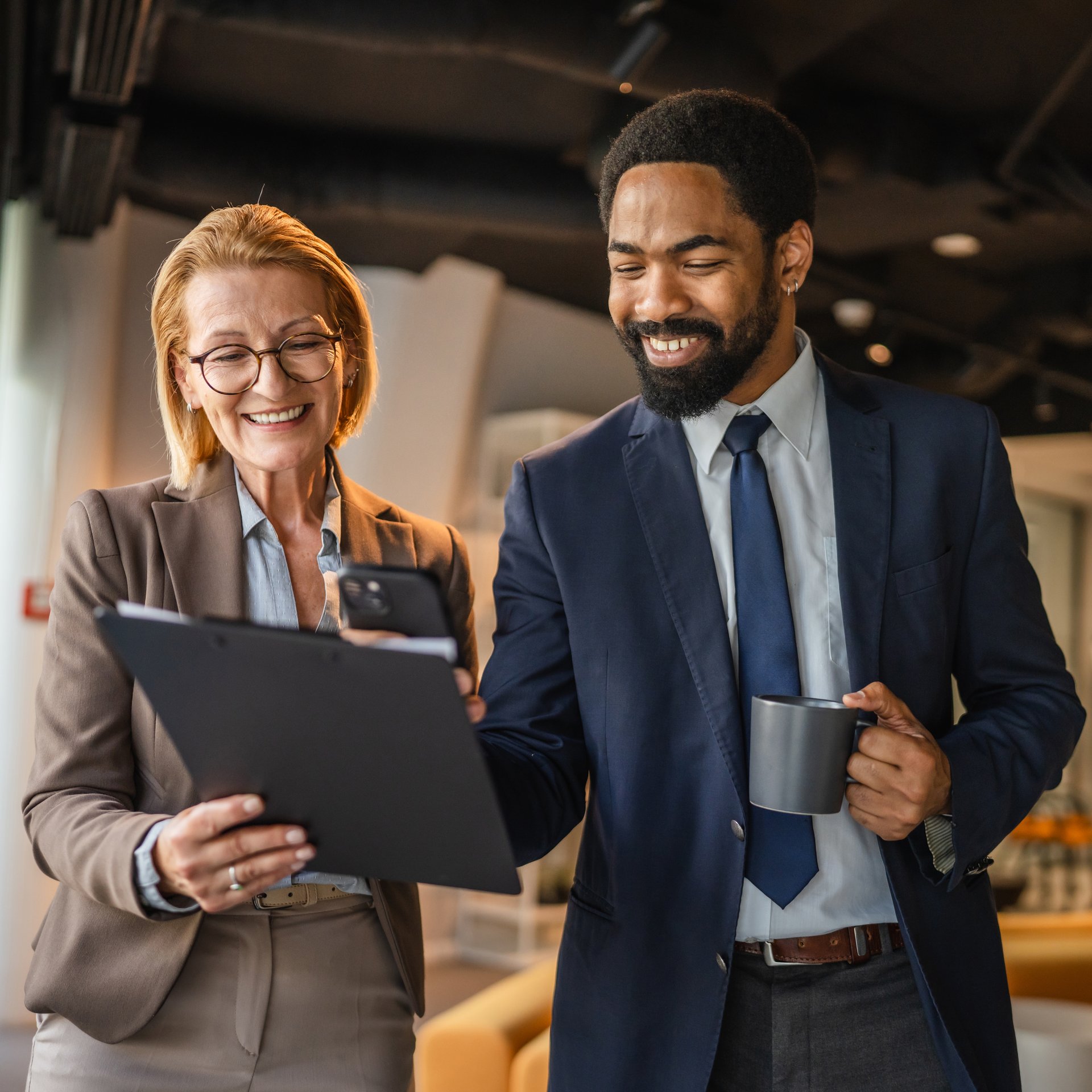 two diverse female and male colleagues review together document files, use mobile phone for scan and take a photo of document