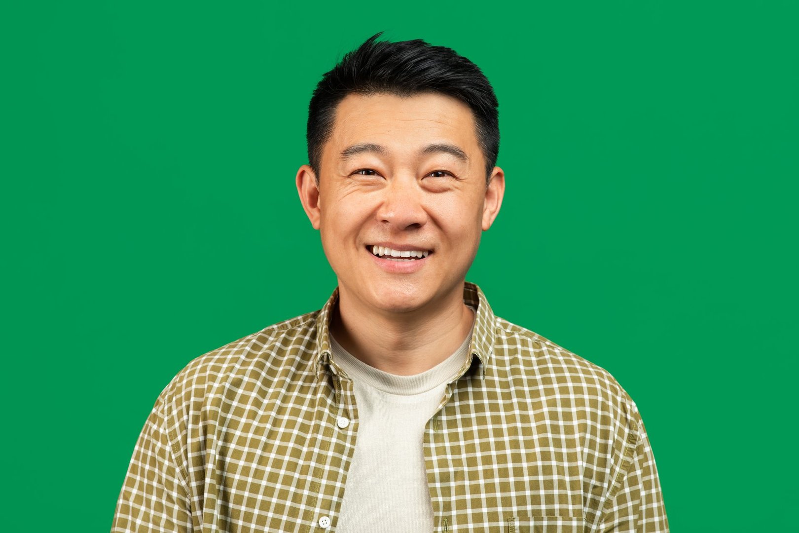 Portrait of positive mature asian man looking and smiling at camera, posing over green background, studio shot. Middle aged man advertising great offer