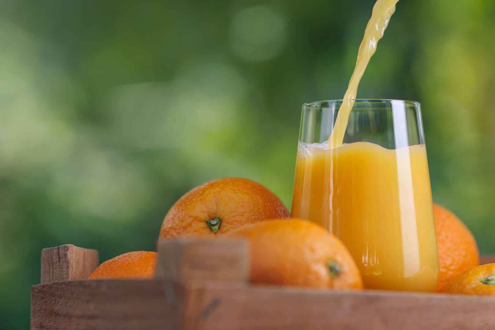 orange juice pouring in glass and ripe fruits near in wooden crate outdoors. Summer refreshing drink
