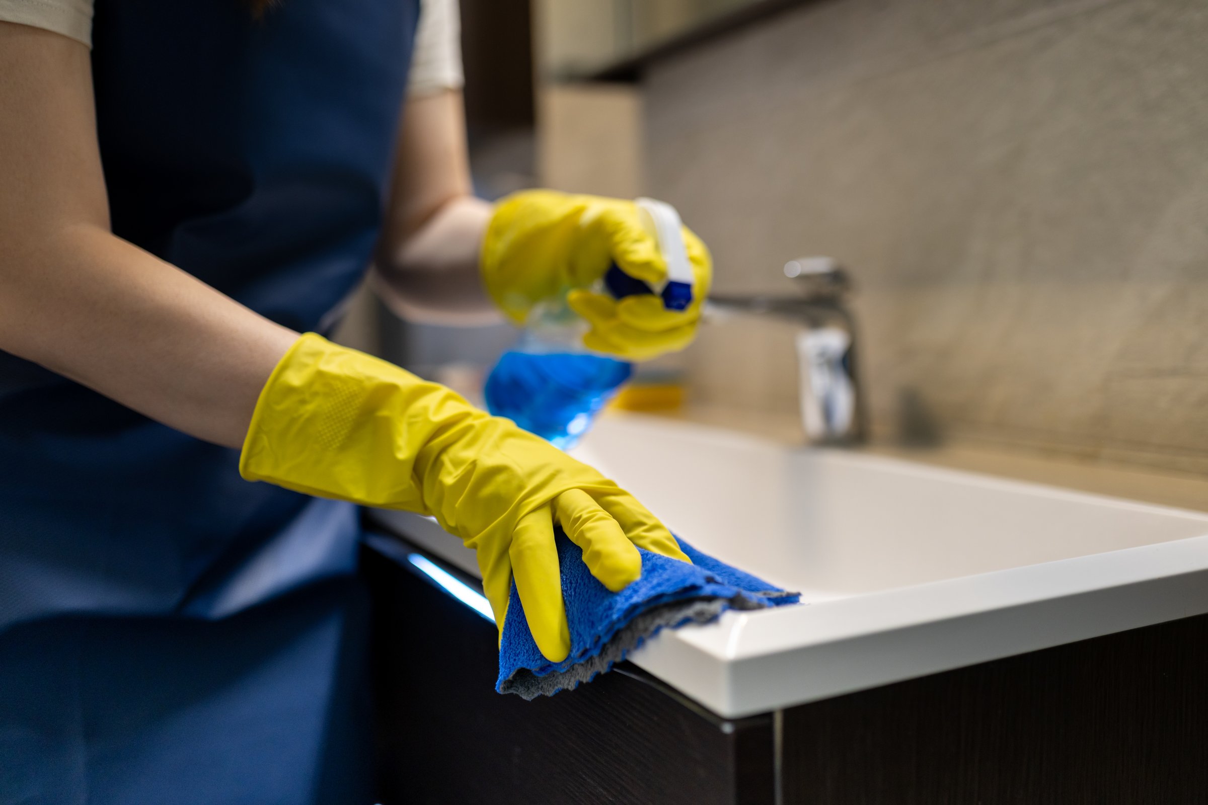 Cleaning a sink using gloves and cloth in a modern bathroom by a diligent person during daylight hours