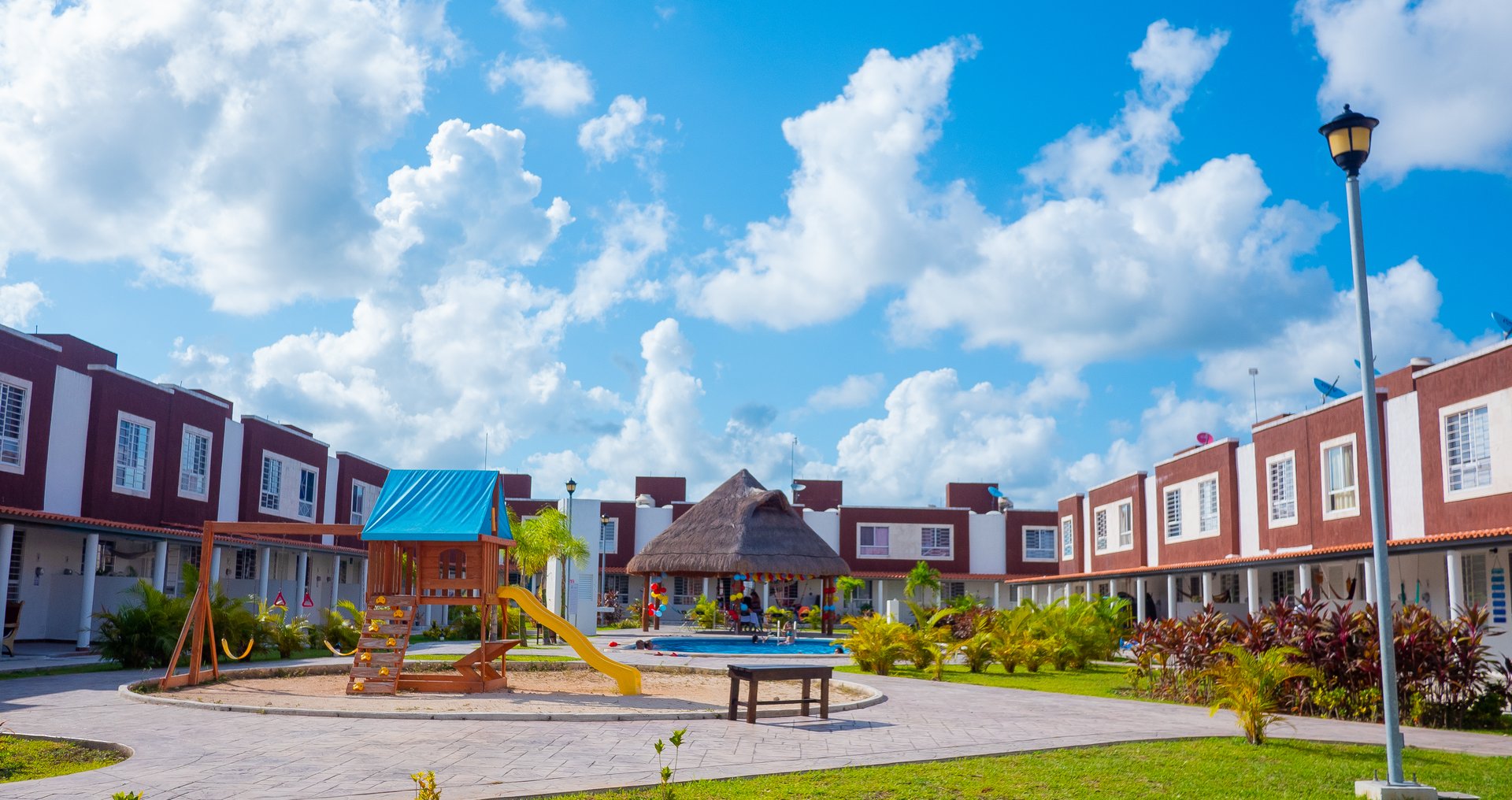 Colorful playground with slide in the center of a housing complex, surrounded by white and red buildings under a blue sky.