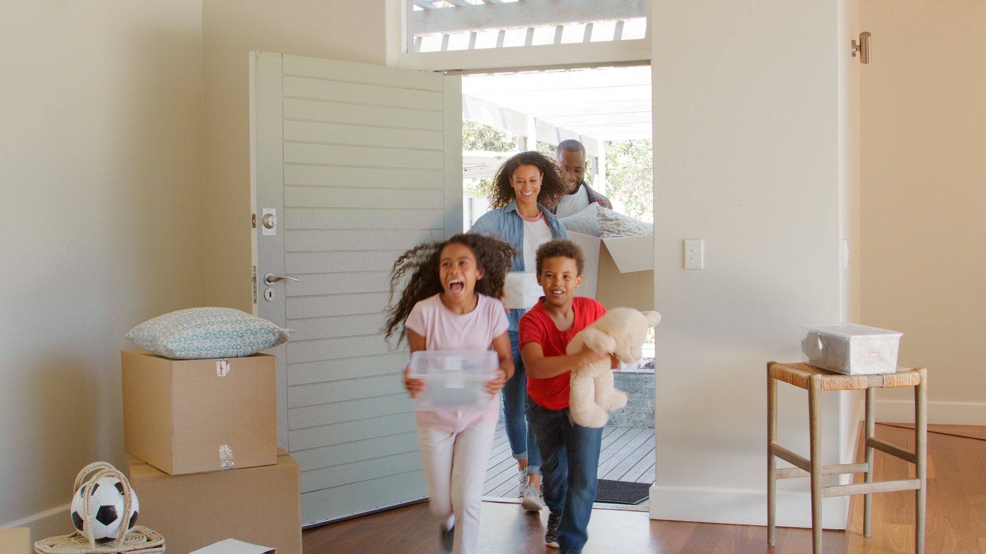 Excited Family Carrying Boxes Through Front Door Into New Home On Moving Day