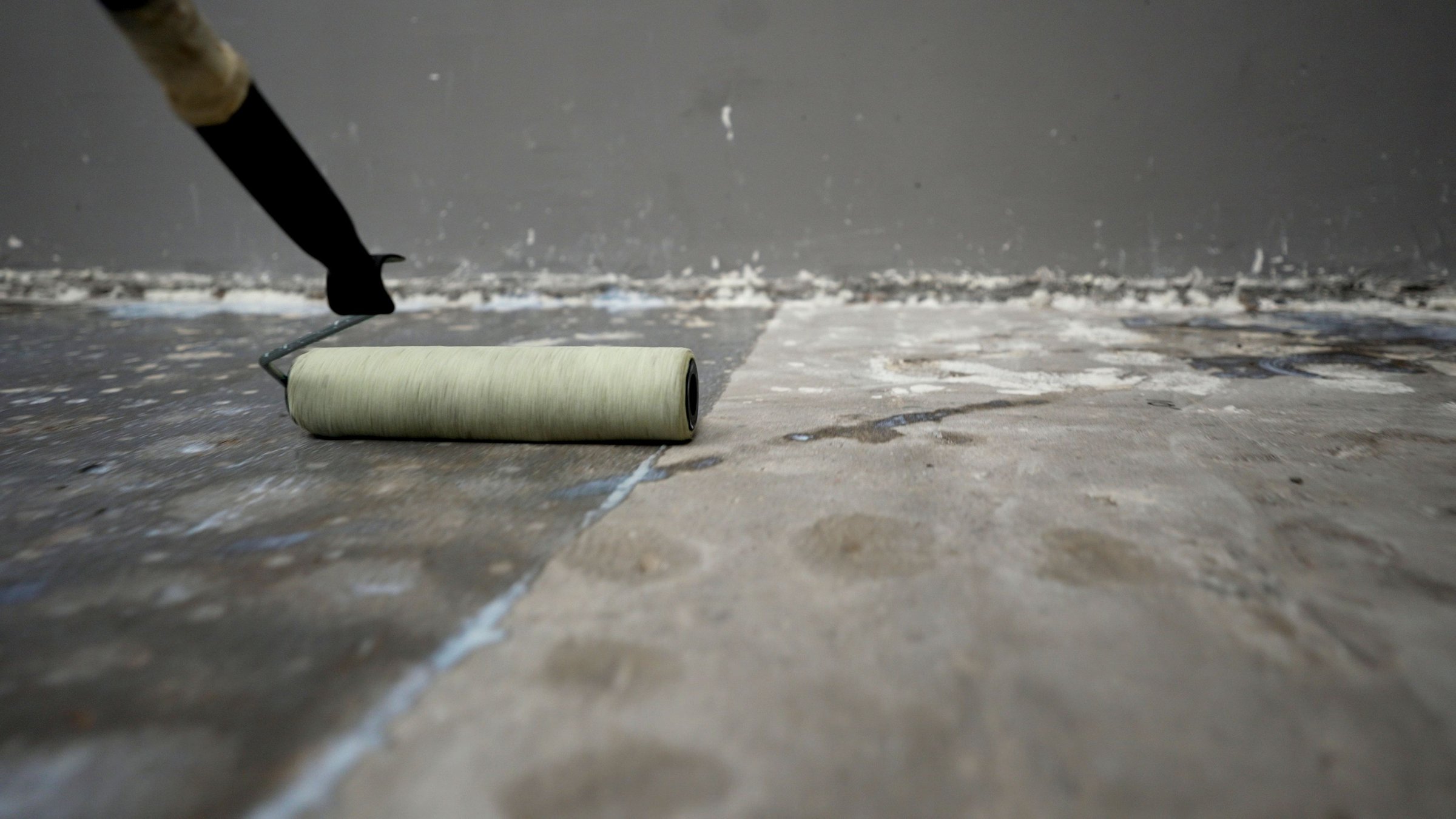 Waterproofing membrane is being applied to concrete floor using paint roller by construction worker during renovation or construction project