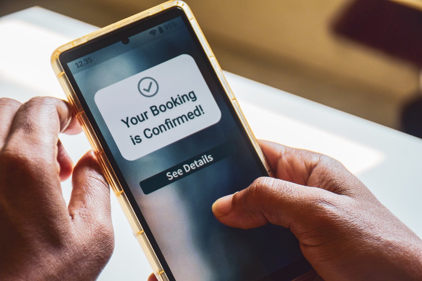 South Asian man holding phone displaying booking confirmation message. Hotel flight or train ticket online booking concept. Selective focus.