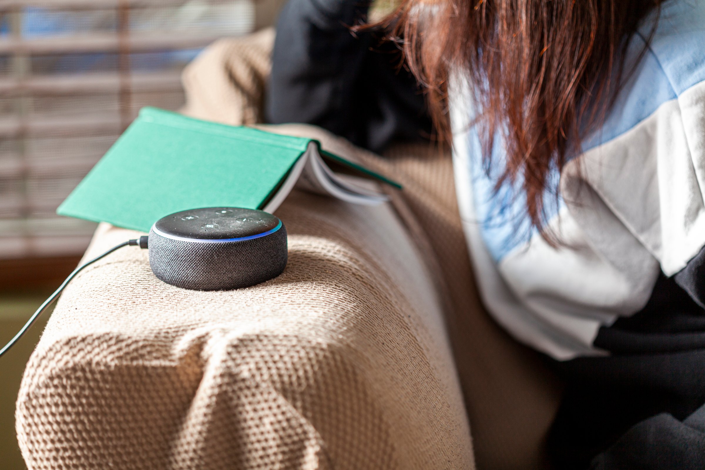 Clarksburg, MD, USA 03-01-2021: A caucasian woman sitting on an armchair with casual clothes in her house is asking a question to Amazon Echo Dot, voice activated speaker device.