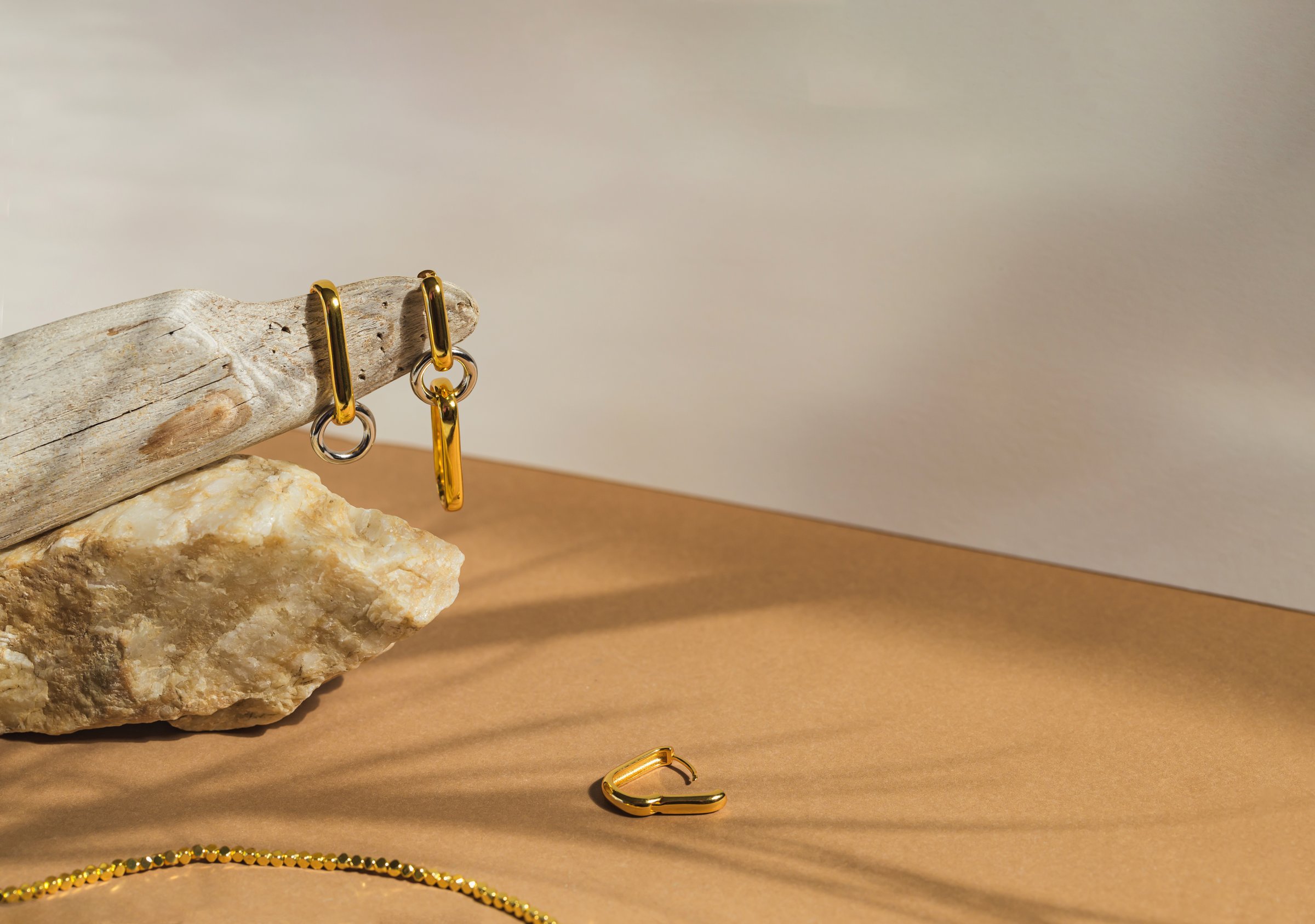 Golden earrings on pastel beige background with shadow. Stylish jewellery set
