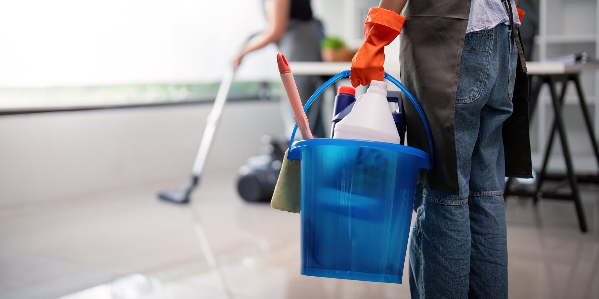 Office cleaner carrying a bucket filled with cleaning supplies while vacuuming, highlighting workplace organization