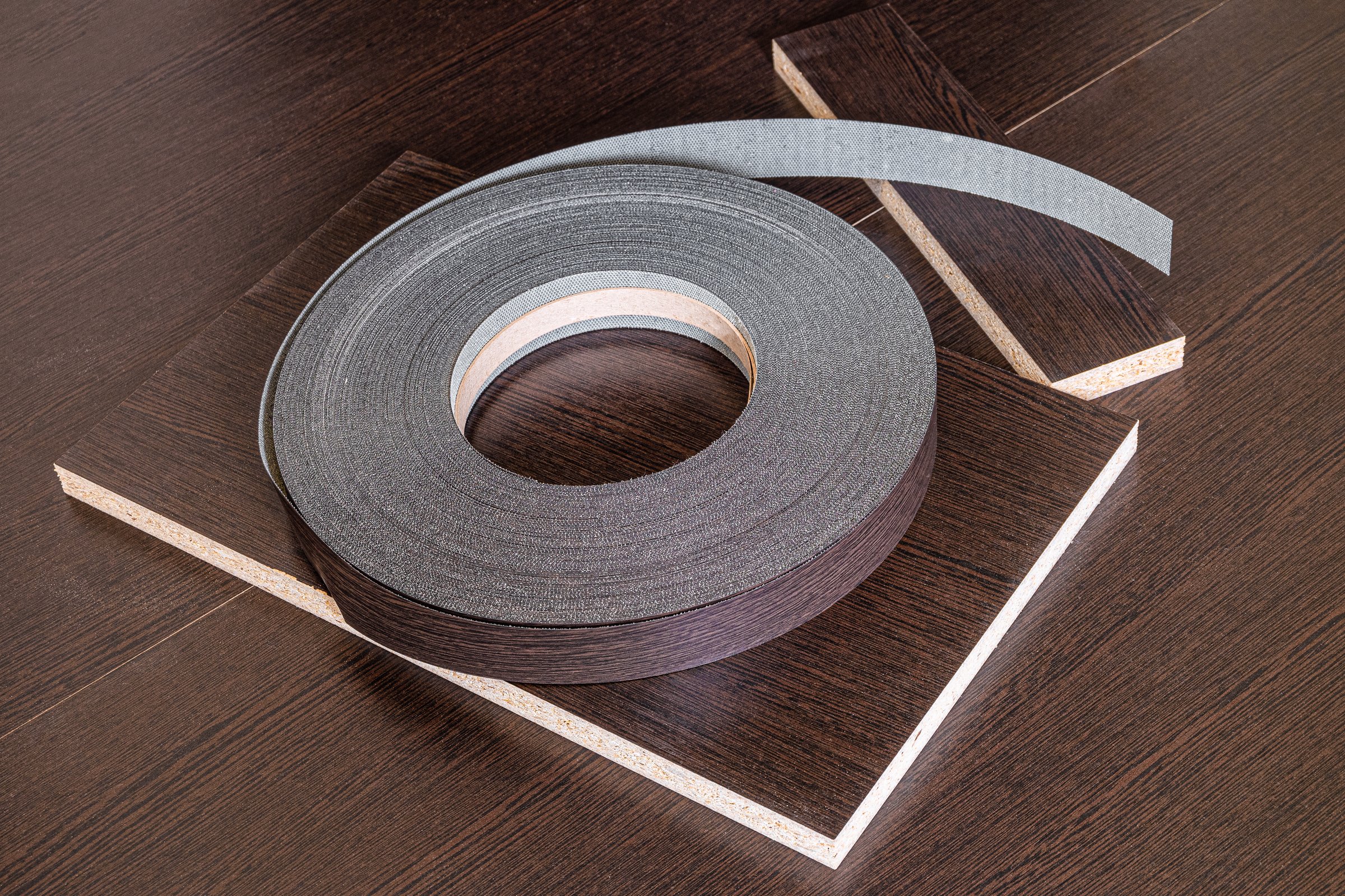 Roll melamine edge for finishing of furniture. Edging tape lying on laminated chipboard sheets wenge color.