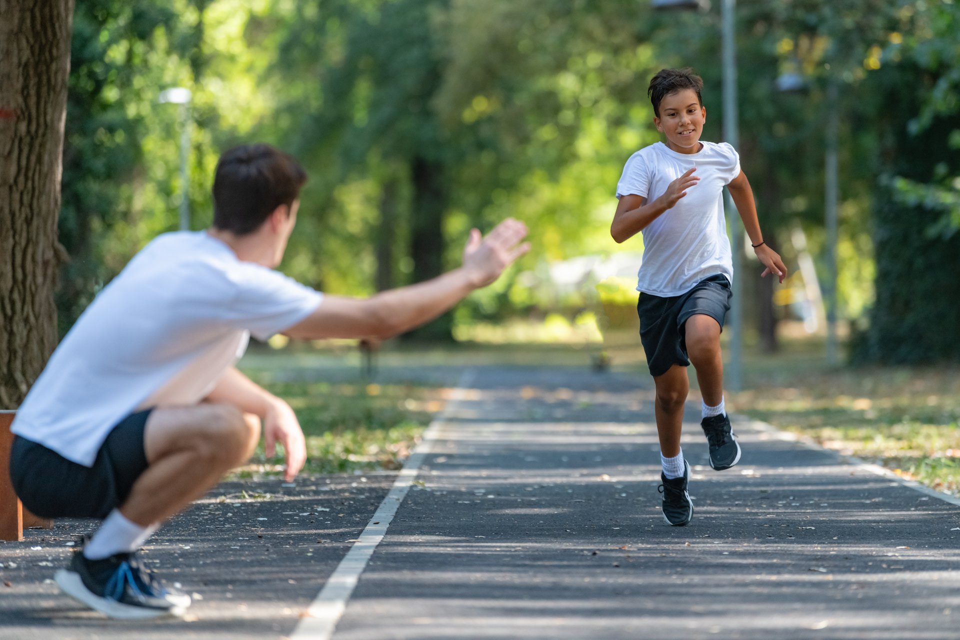 Trainer helps a young boy practice speed running in a park, focusing on technique and fitness. The boy is actively engaged, enhancing his athletic skills in a natural outdoor environment.