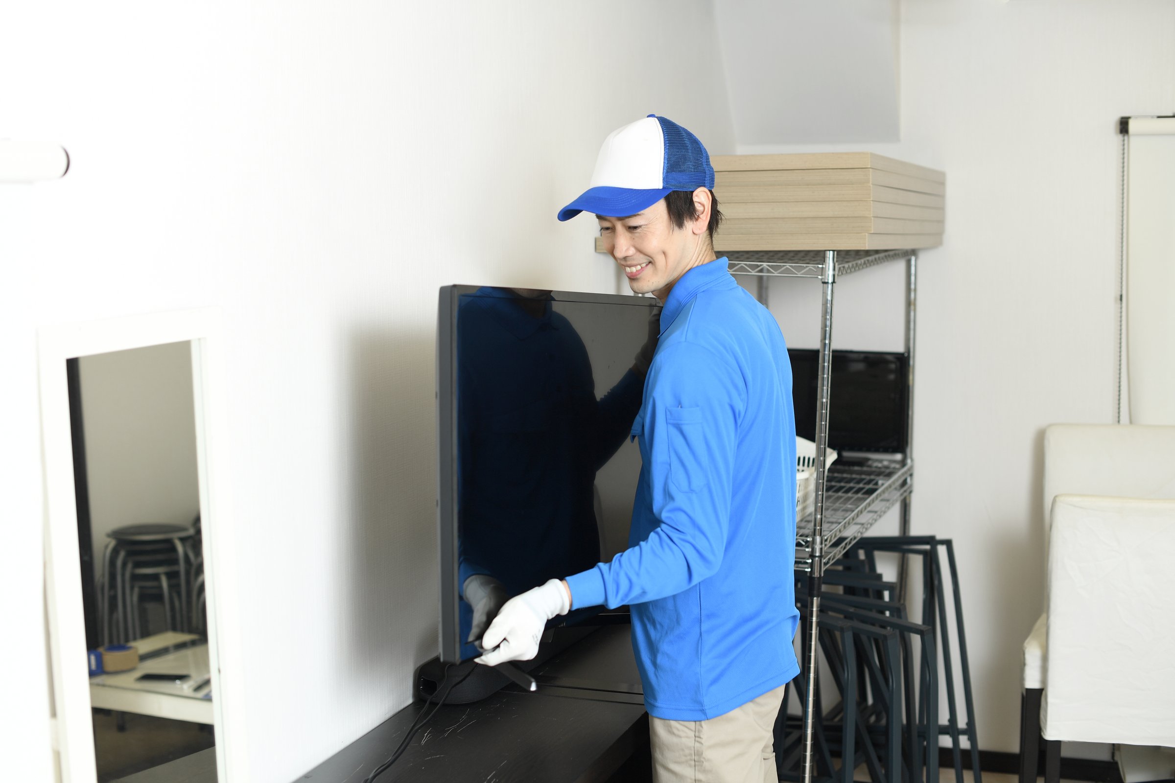 An Asian male worker holds a television in the living room of a house.