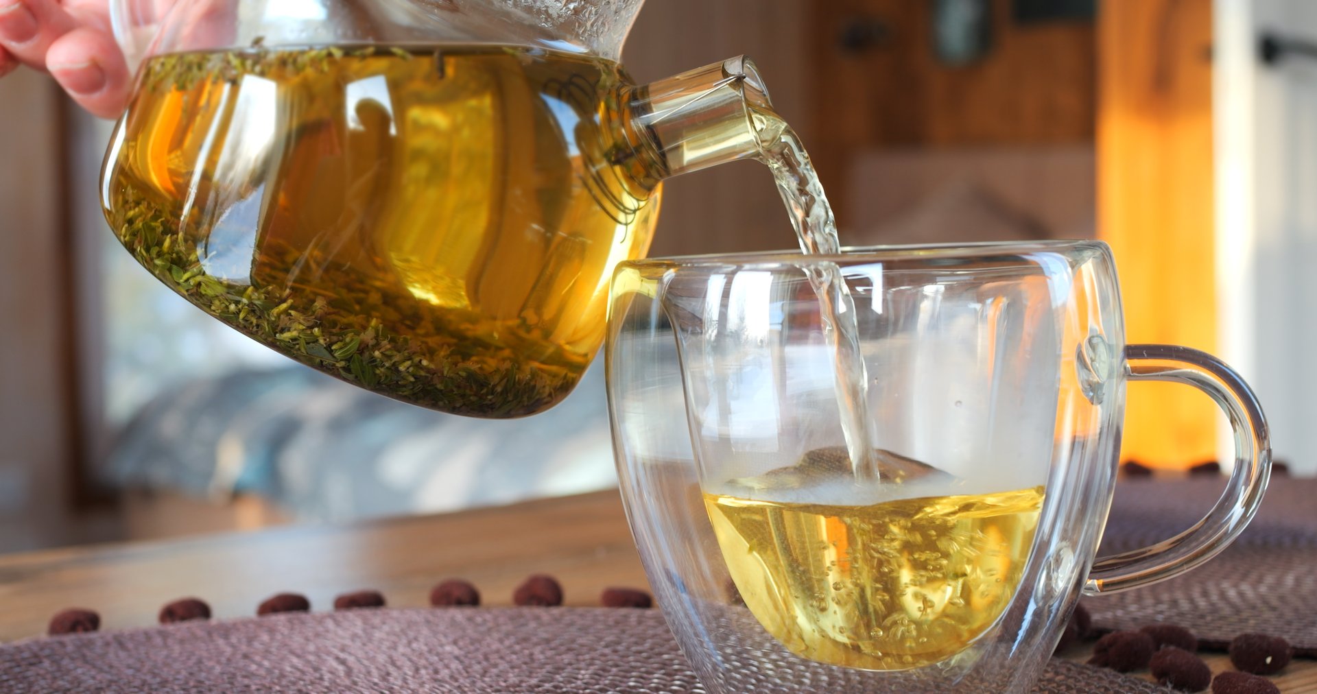 Tea drink is poured from teapot into glass mug on table. Morning tea ceremony, moment of pleasure. Experience tea ceremony as moment of pure pleasure. Classic morning tea ceremony concept.