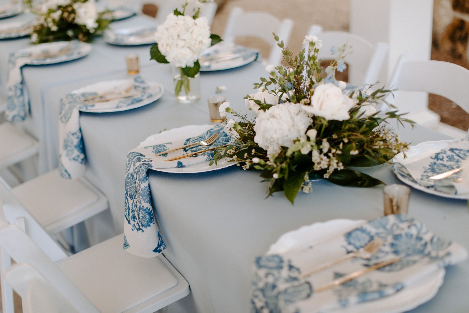 Elegant table setting with floral centerpiece and blue patterned napkins for a wedding reception.