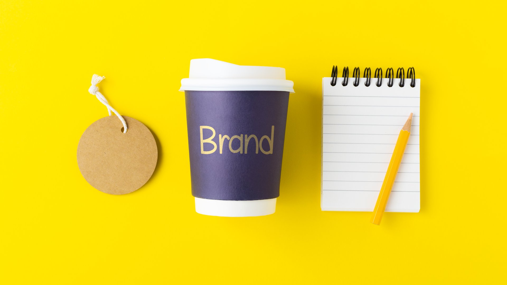 Coffee brand identity concept with brand word on coffee cup with tag label and notebook, mockup on yellow background