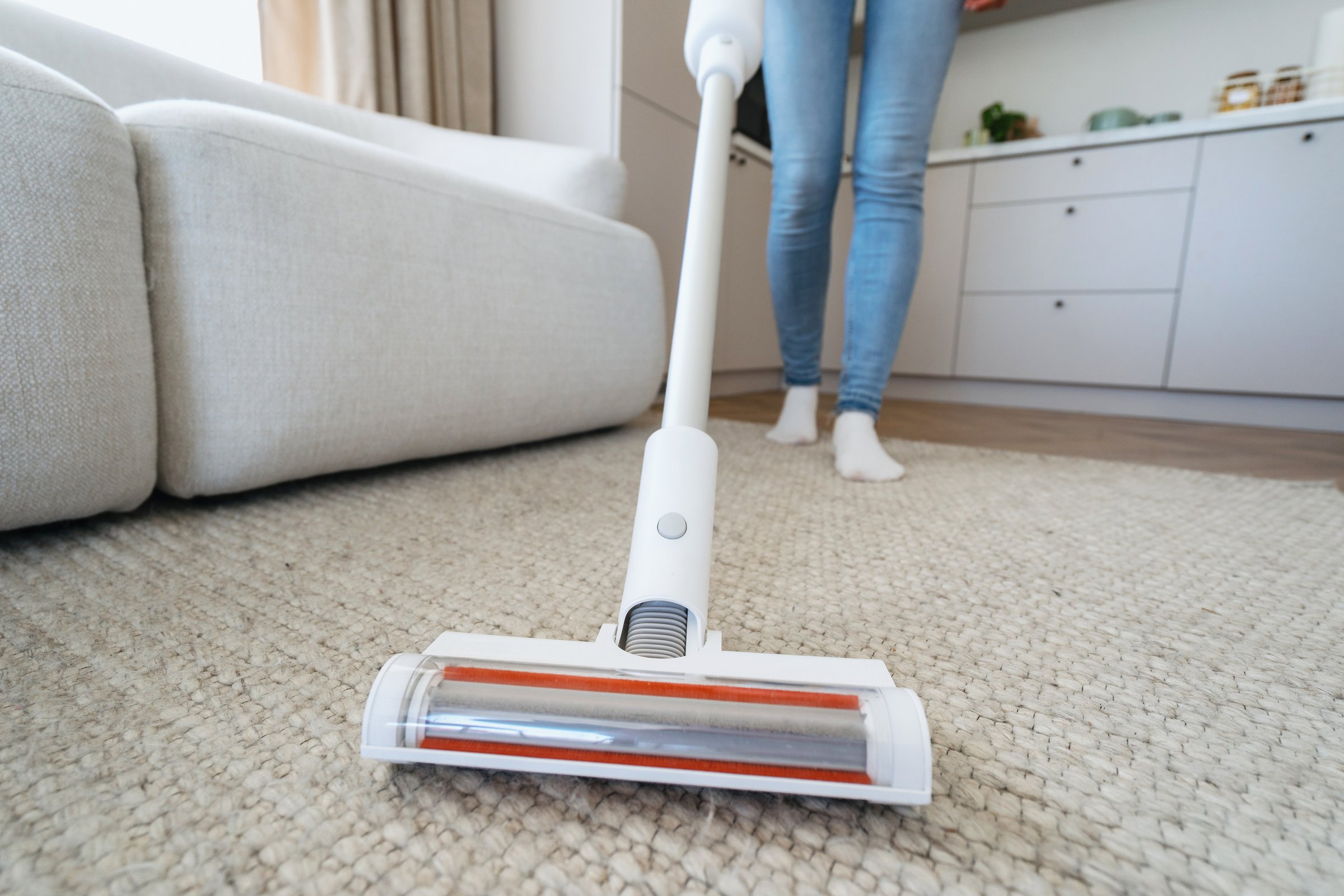 Housework and housekeeping concept. Selective focus at brush on modern and cordless vacuum cleaner. Cropped woman using professional appliance to hoovering carpet at home