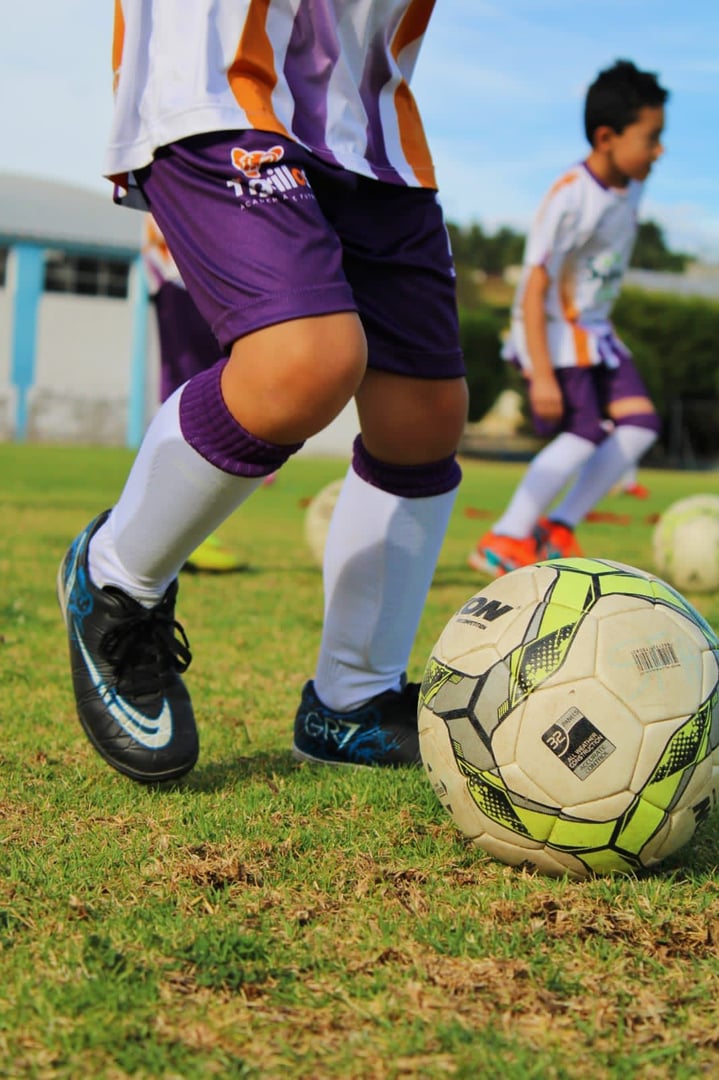 Children in soccer uniforms practicing with a ball on a grassy field.