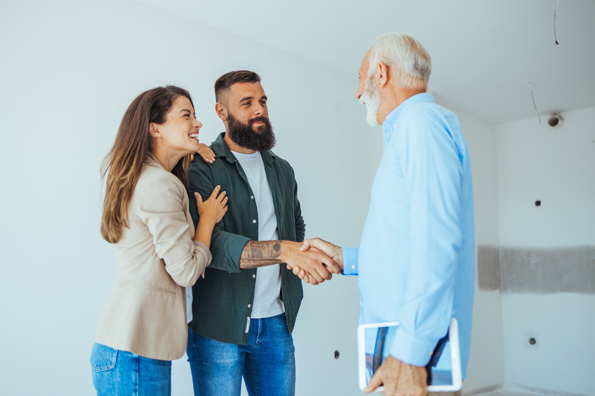 Lovely married couple, looking to buy a new apartment with a help of a real estate agent. Real Estate Agent showing a house under construction to a couple and greeting them with a handshake